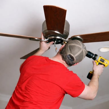 Man installing a ceiling fan with a power drill.