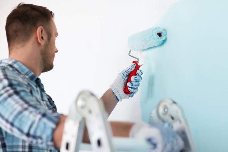 Man painting wall with roller in light blue color