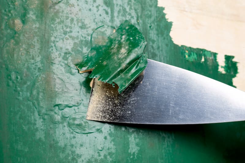 Metal scraper removing green paint from surface