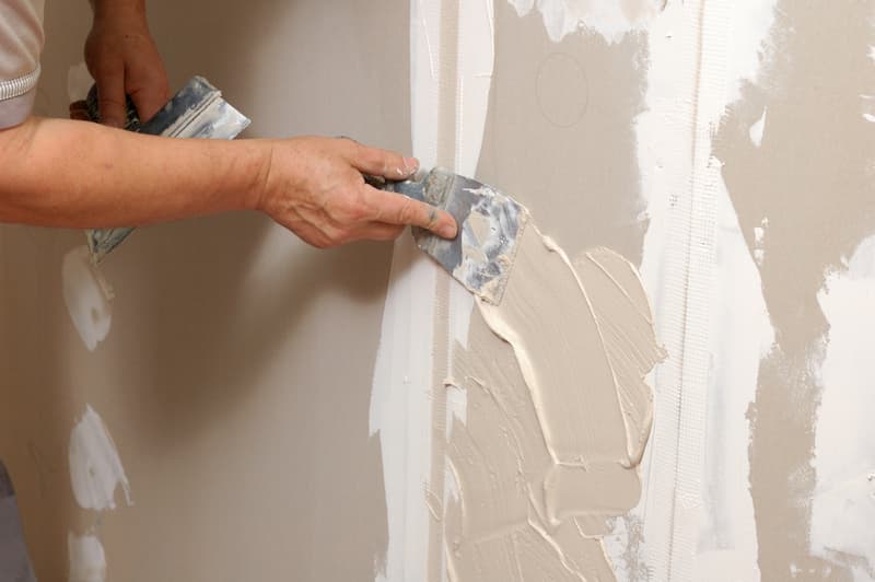 A worker using a putty knife to apply plaster on a wall.